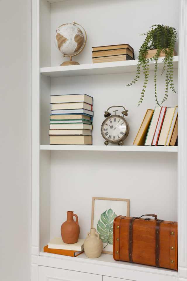 vertical white shelving in home office nook with artwork, books and greenery